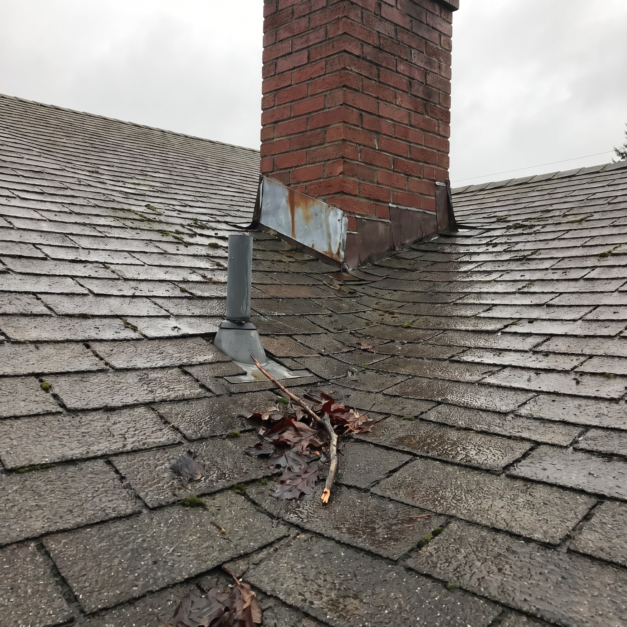 Weathered roof flashing around a brick chimney and plumbing vent after recent storms