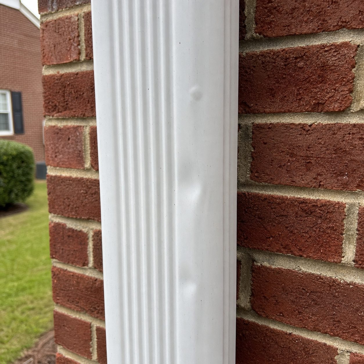 Subtle shallow dents on a white metal residential downspout