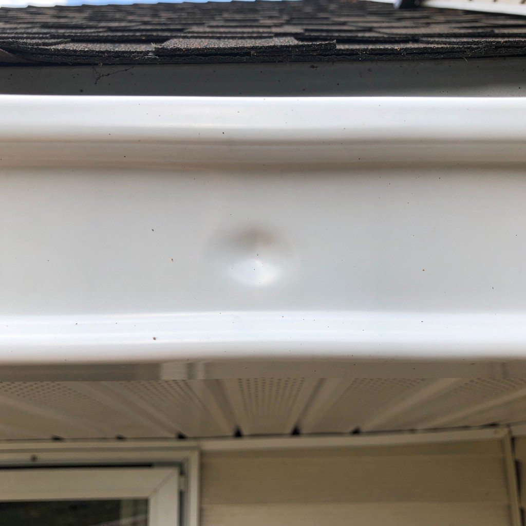 Close view of a light-colored metal gutter with a shallow dent on the front face