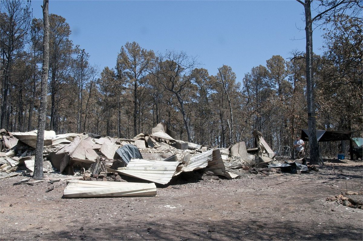 Wildfire-destroyed residential home with collapsed building materials, debris, scorched ground, and burned trees