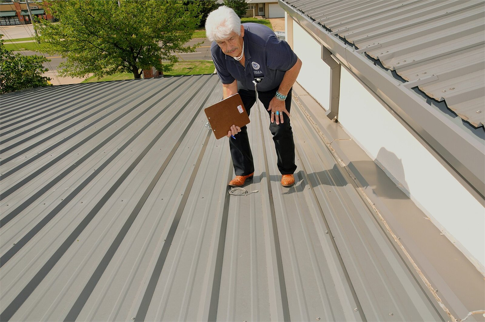FEMA public assistance officer documenting roof conditions on a standing-seam metal roof in Oklahoma