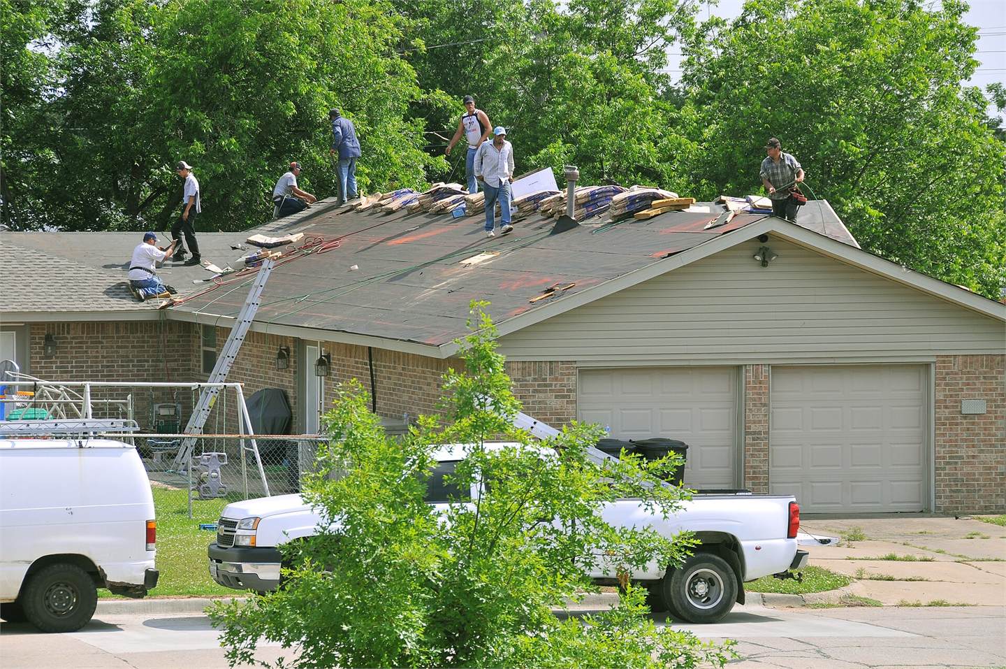 Residential asphalt-shingle roof repair in progress with workers, underlayment, material bundles, ladders, and the home visible