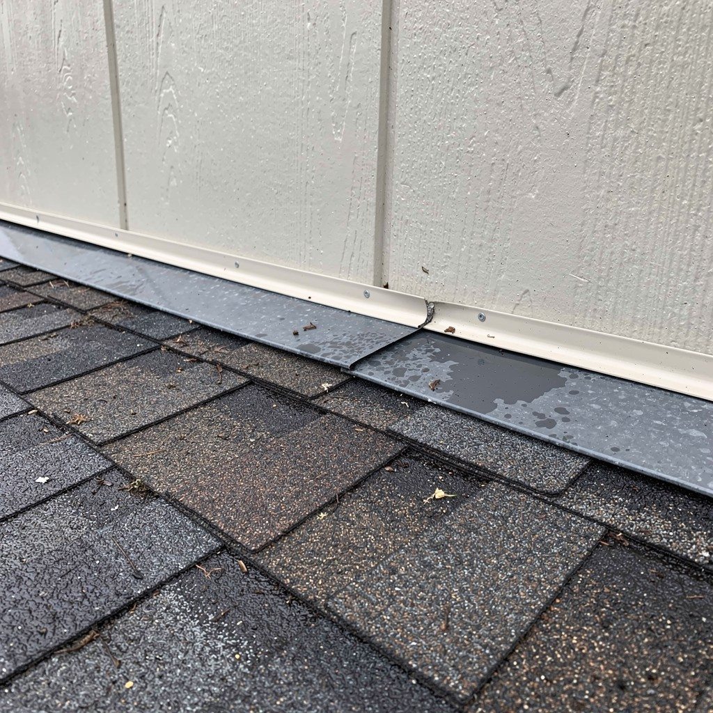 Wet asphalt shingles and roof-to-wall flashing at a residential wall intersection after recent storms