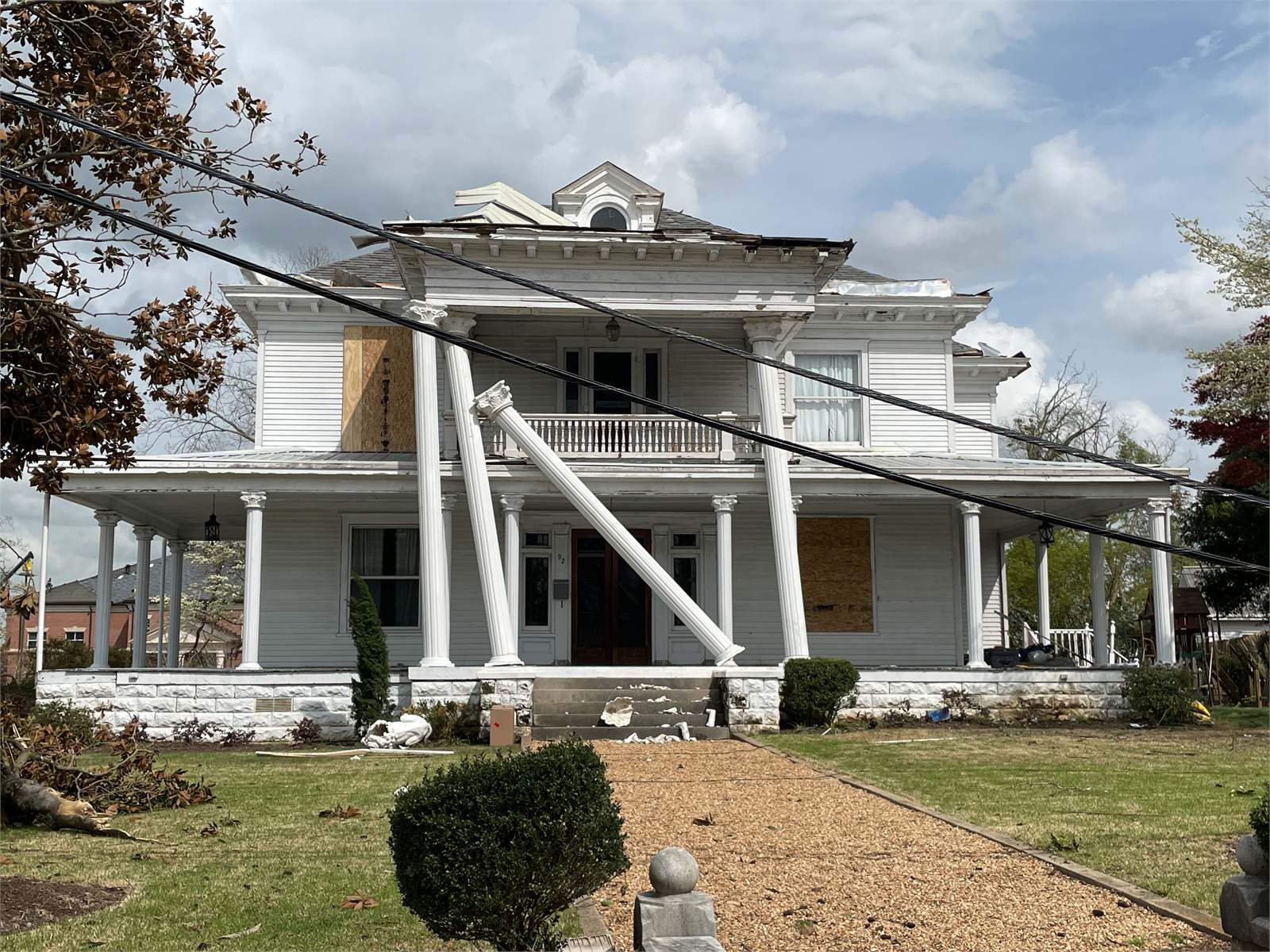 Georgia residence with a lifted roof edge, boarded openings, damaged porch columns, displaced trim, and scattered material after recent severe weather
