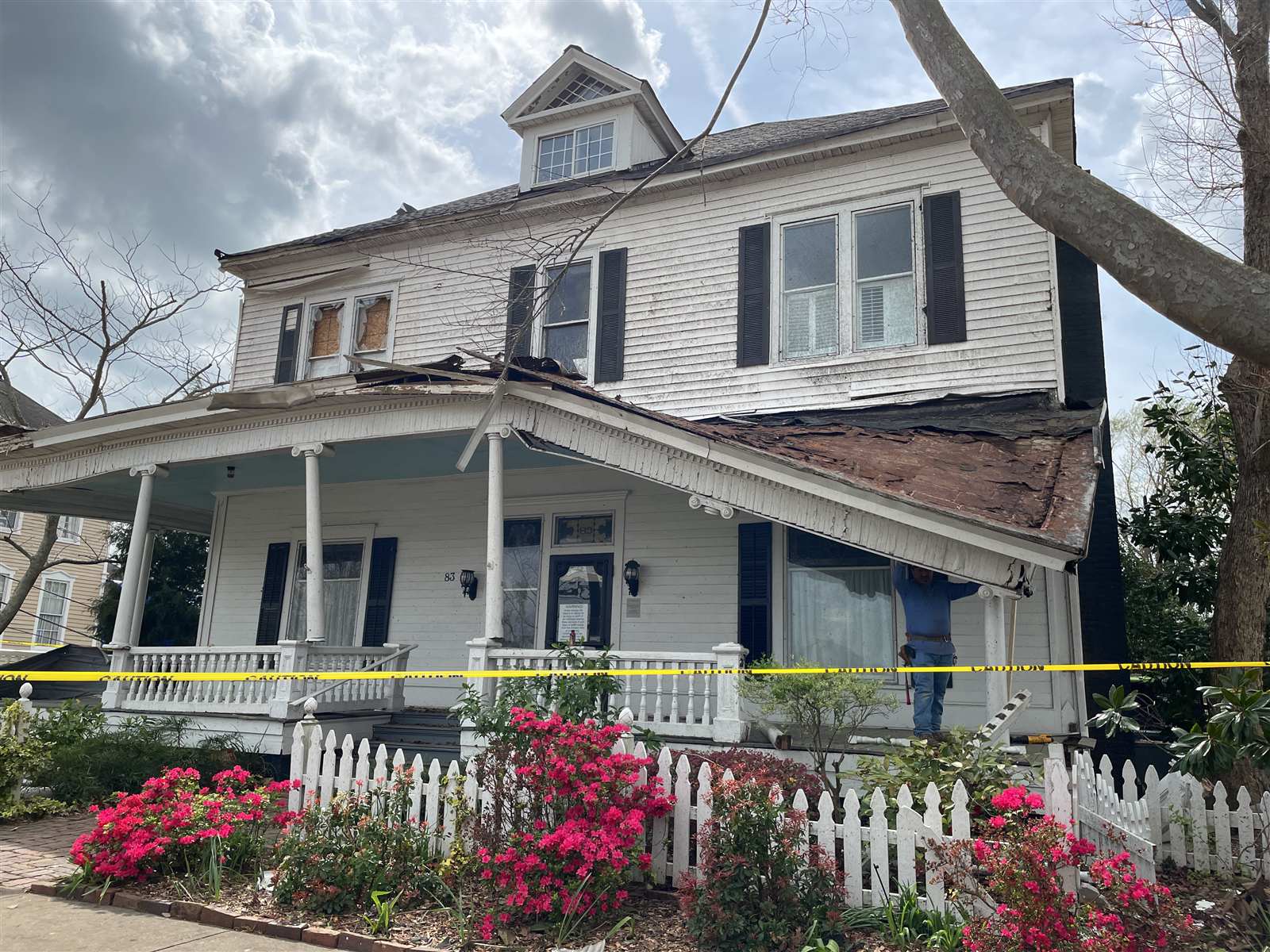 Georgia residence with a lifted roof edge, boarded openings, damaged porch columns, displaced trim, and scattered material after a severe wind event