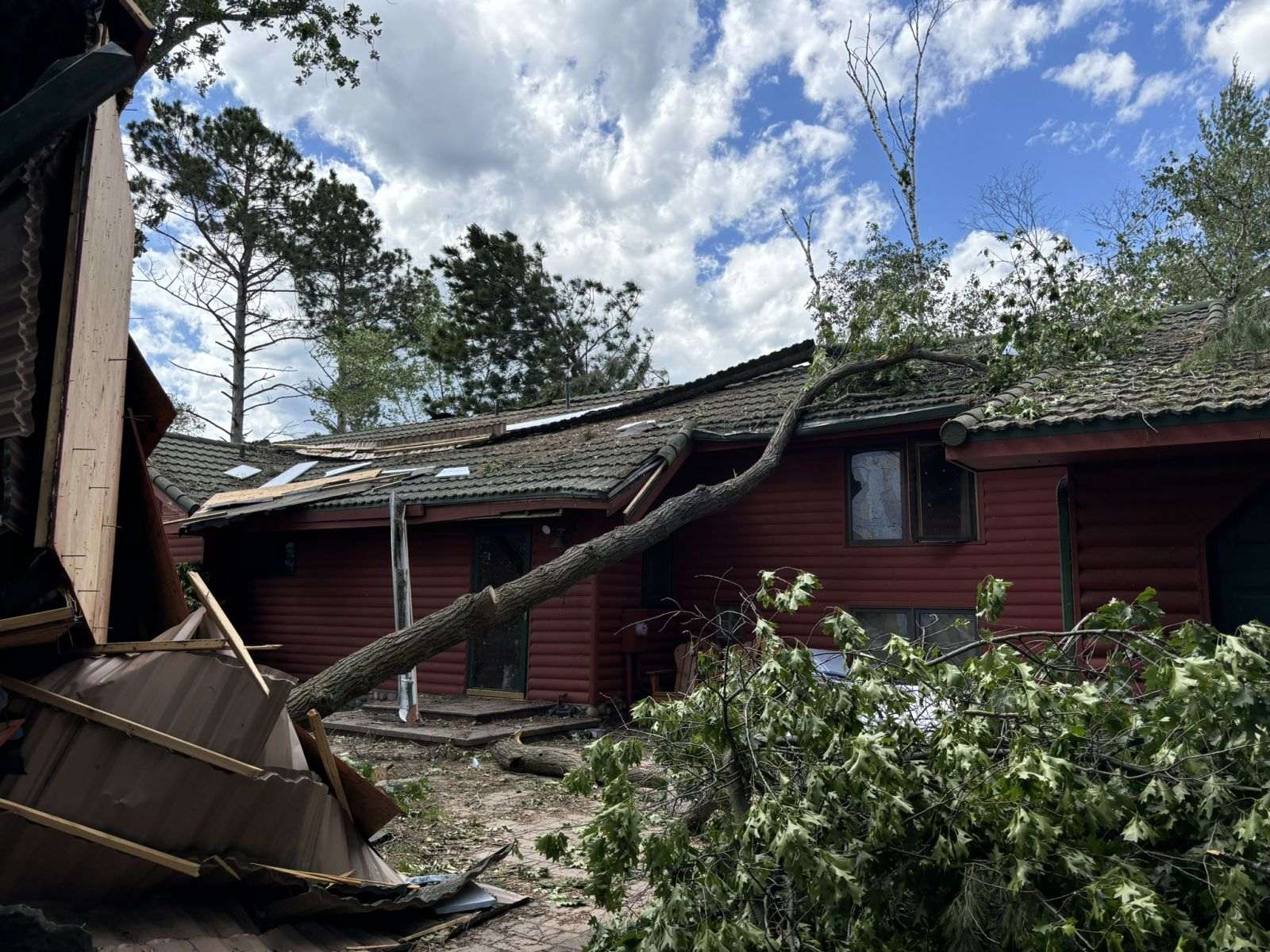 Fallen tree across a residential roof with damaged roof sections and storm debris in an NWS Duluth storm-survey photograph