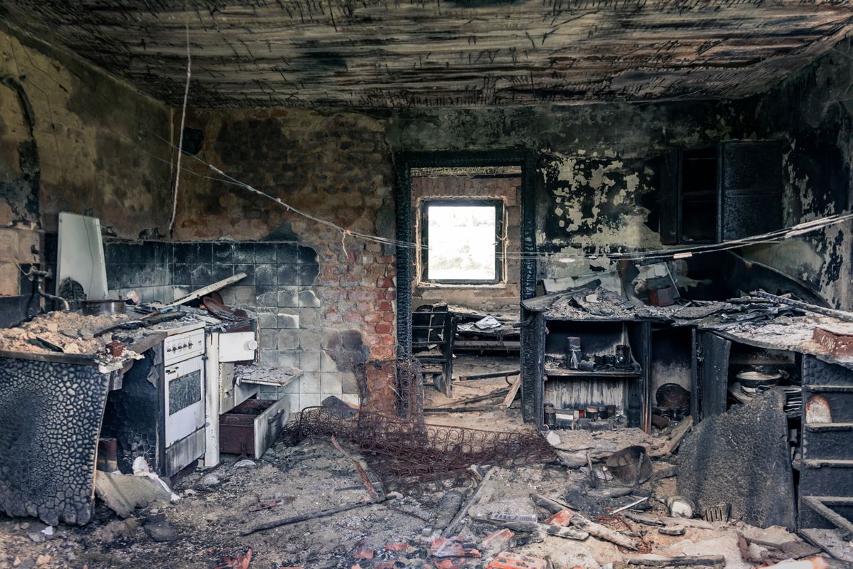 Fire-damaged residential kitchen with charred ceiling, soot-blackened walls, damaged cabinets, and debris