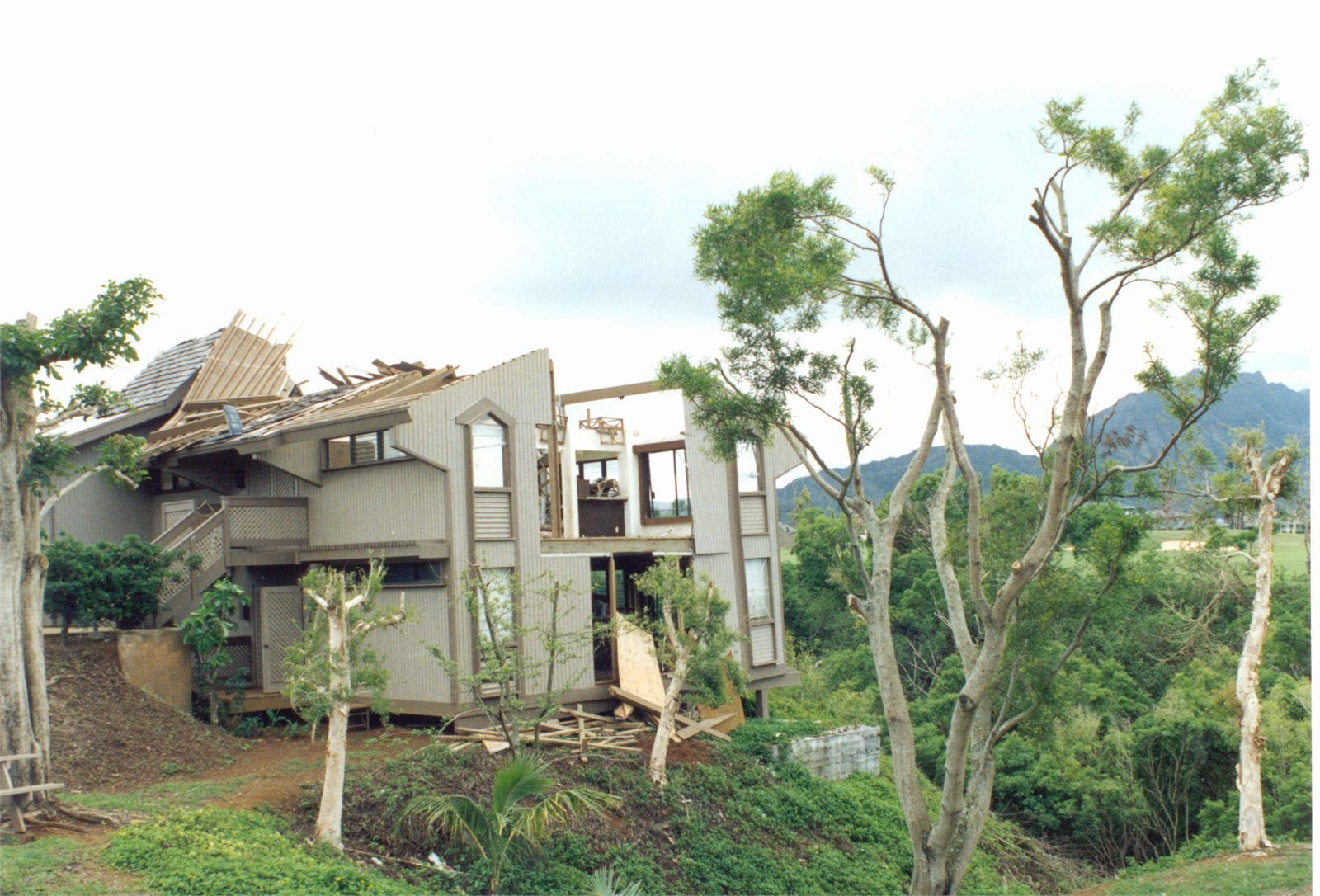 Residence with large roof and upper-floor sections torn away by wind, exposing framing and interior rooms