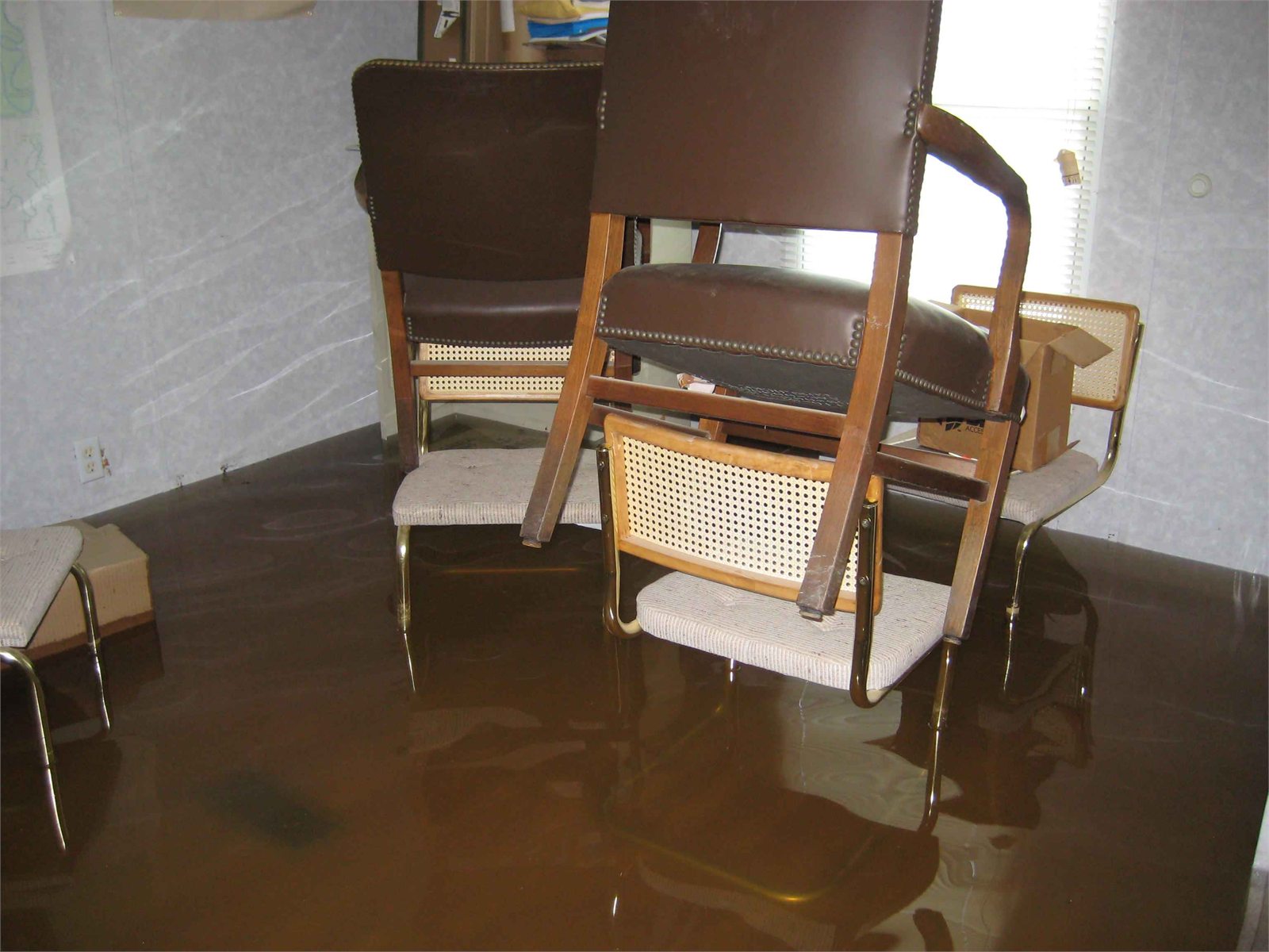 Flooded residential interior with standing water, raised furniture, chairs, and room surfaces