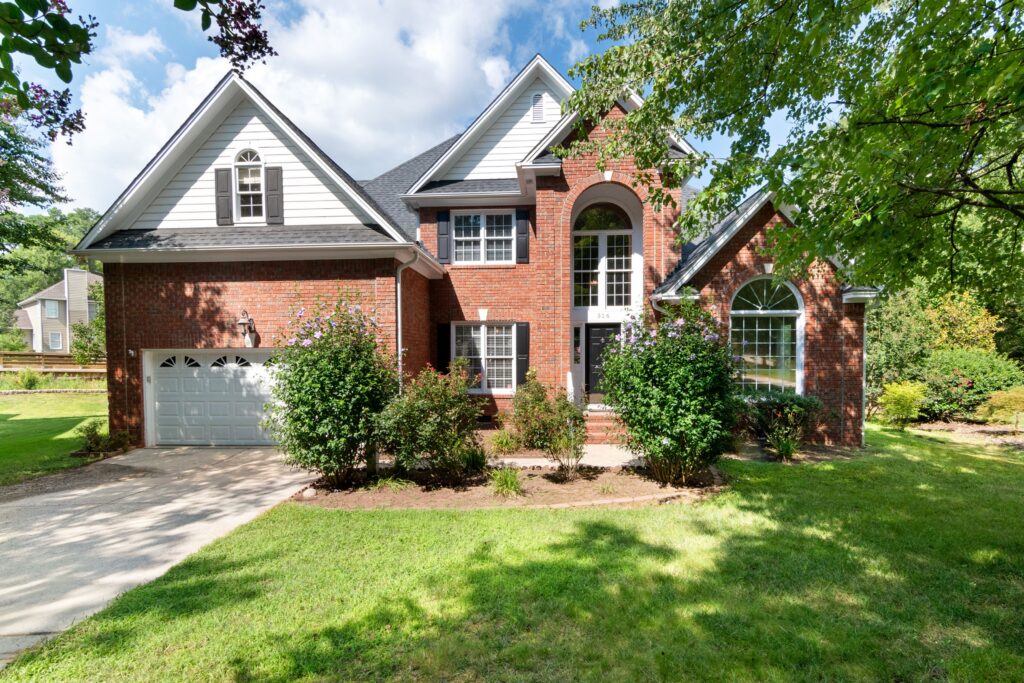 A brick home with a shingle roof, driveway, lawn and trees. Illustrative stock property.