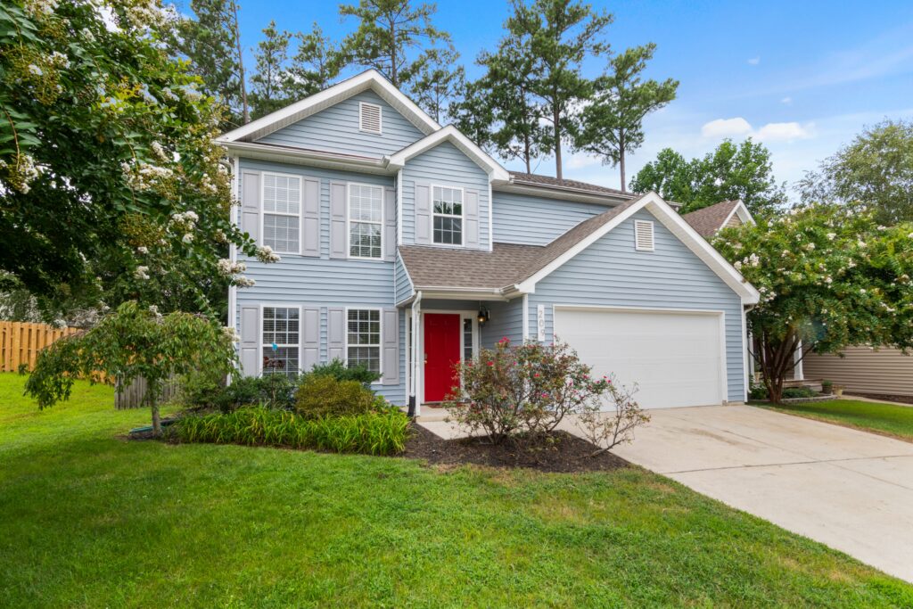 A blue two story home with a shingle roof, lawn, driveway and trees. Illustrative stock property.