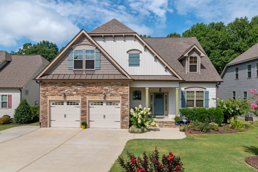 A complete suburban home with stone facing, two garage doors and a shingle roof. Illustrative stock property.