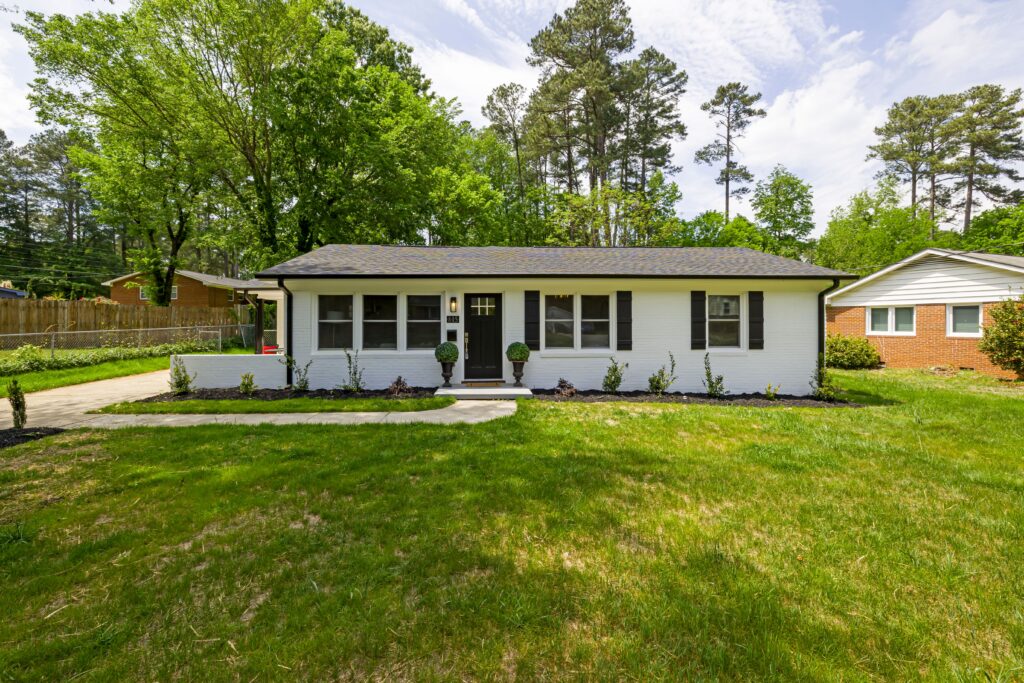 A white single story home with a shingle roof, lawn and trees. Illustrative stock property.