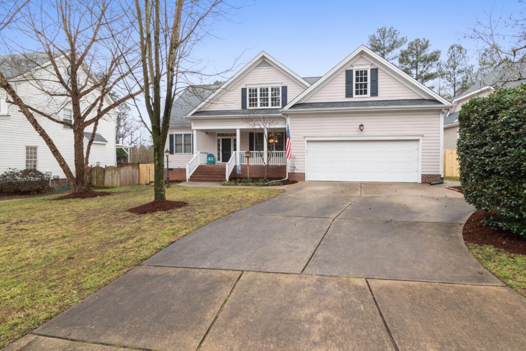 A light colored suburban home with a shingle roof, front porch, garage and yard. Illustrative stock property.