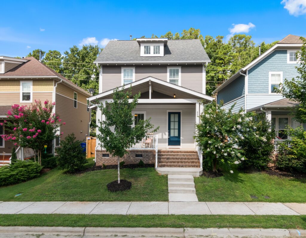 A gray home with a shingle roof, front porch, lawn and neighboring homes. Illustrative stock property.
