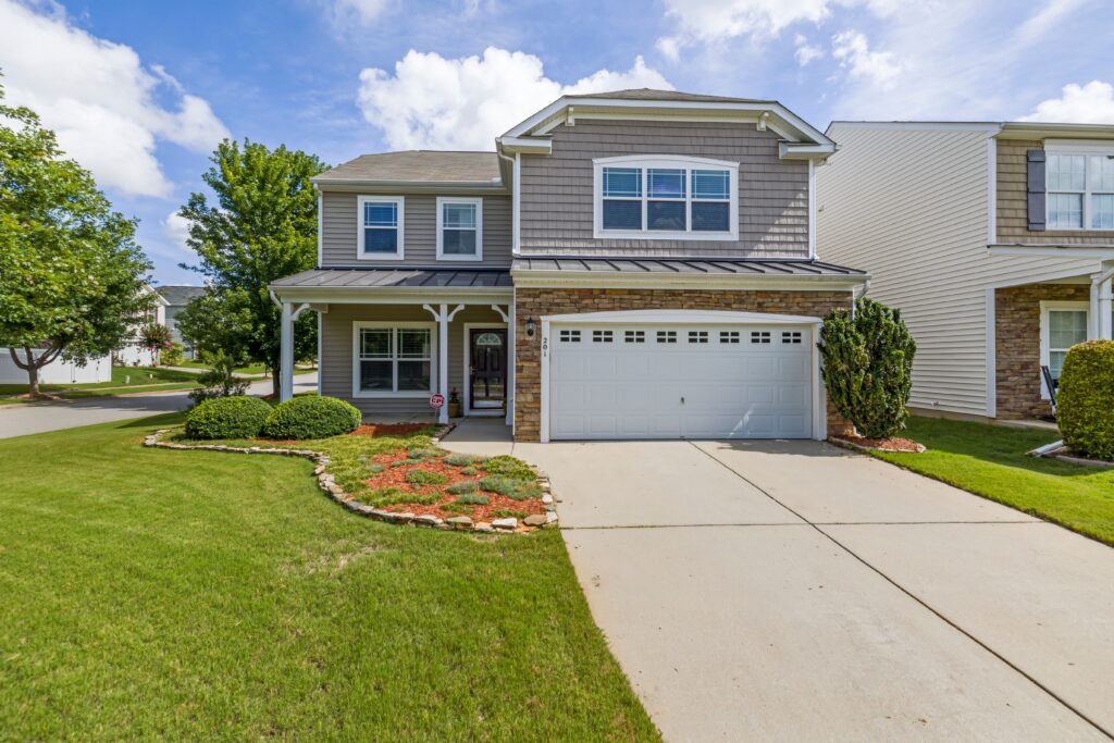 A two story suburban home with a shingle roof, porch, lawn and driveway. Illustrative stock property.